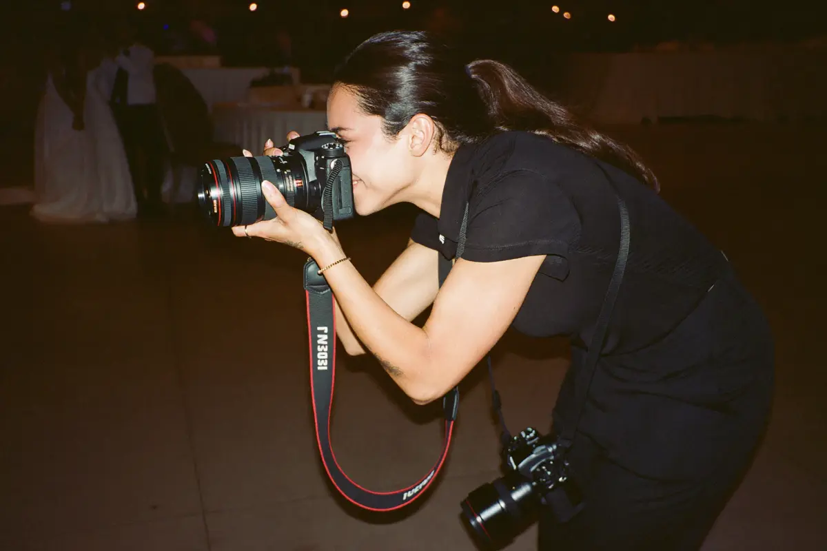 Una fotógrafa profesional vestida de negro trabajando con su cámara durante una boda, con una segunda cámara colgada al hombro