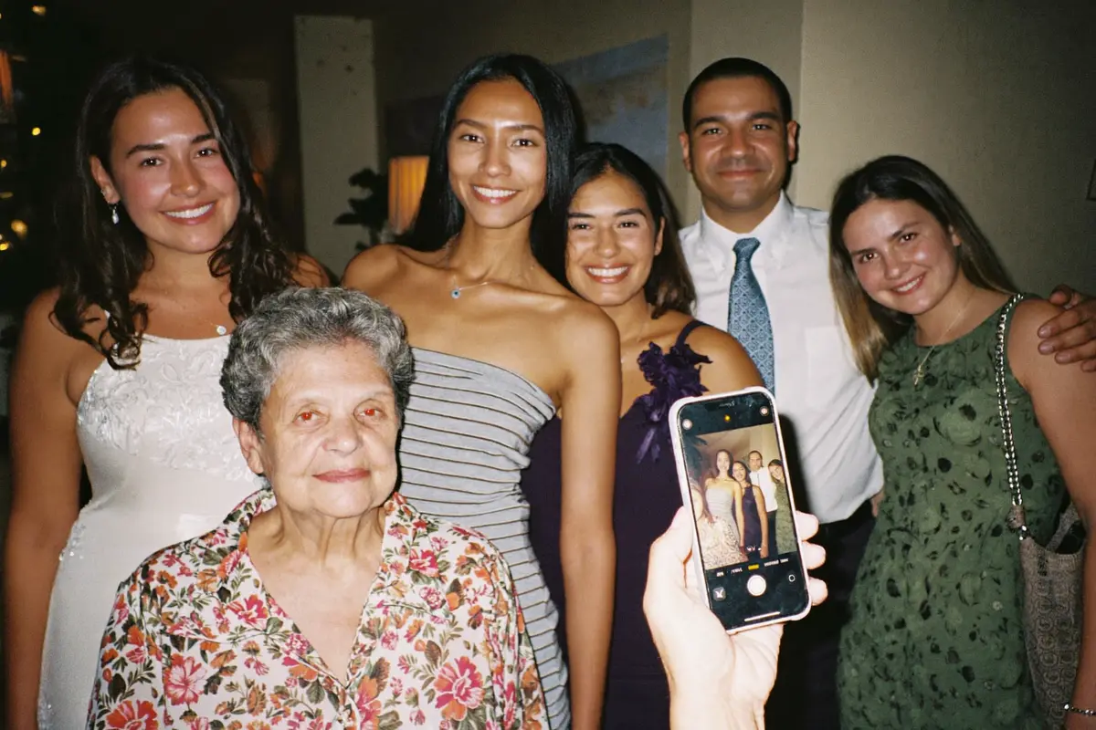 Una familia de varias generaciones posando junta en una fiesta mientras una de ellas toma la foto con su celular, con la abuela al frente