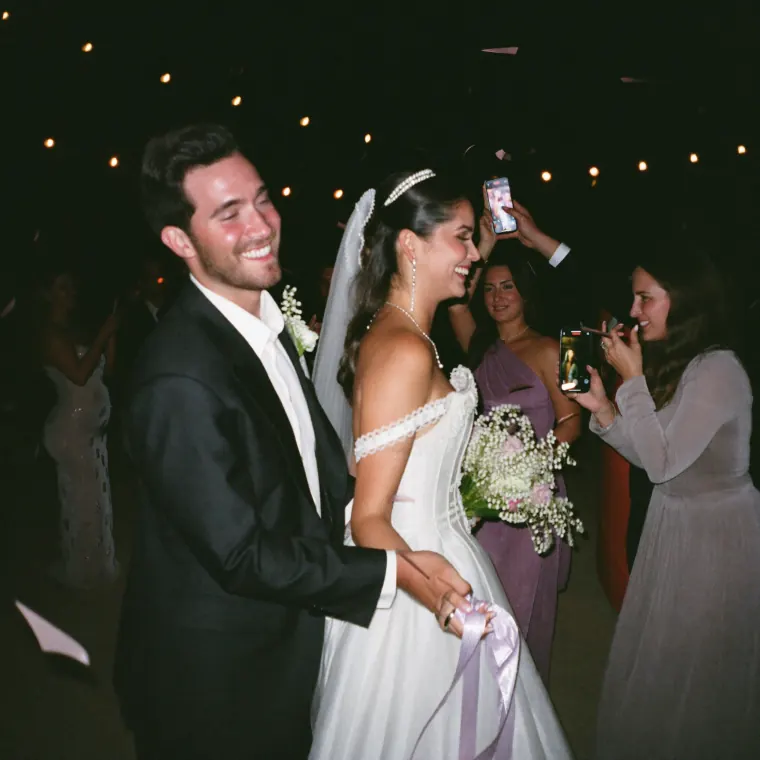 Los novios caminan sonriendo entre sus invitados, que los graban con los celulares en alto.