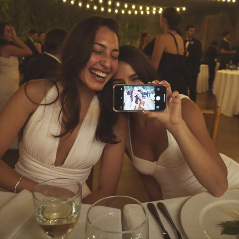 Dos amigas ríen juntas mirando una foto en la pantalla del celular durante la fiesta.