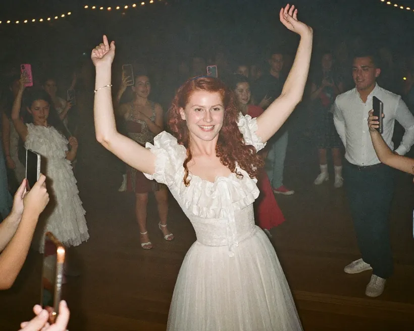 La quinceañera baila con los brazos en alto en la pista mientras sus invitados la graban con los celulares alrededor.
