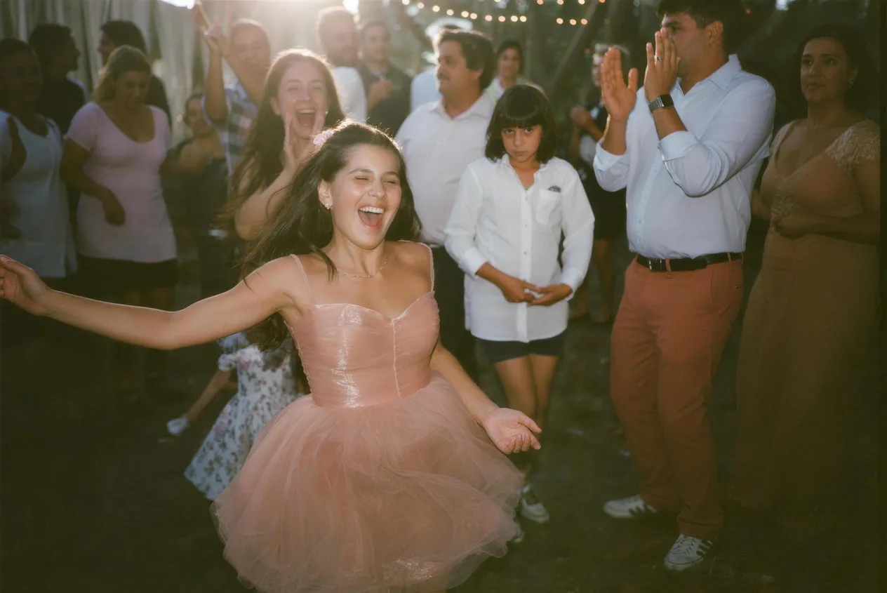 Quinceañera bailando al caer la tarde, rodeada de invitados que aplauden y ríen bajo luces de feria